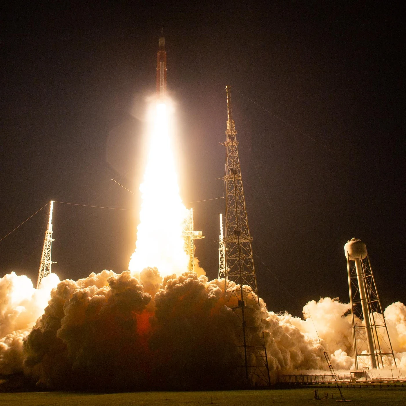 The SLS rocket launches at night above bright exhaust and clouds.