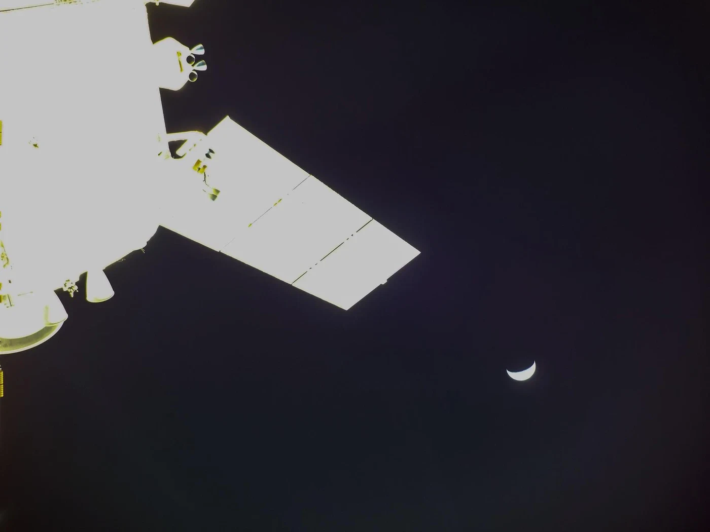 Orion spacecraft hardware with a crescent Moon against black space.