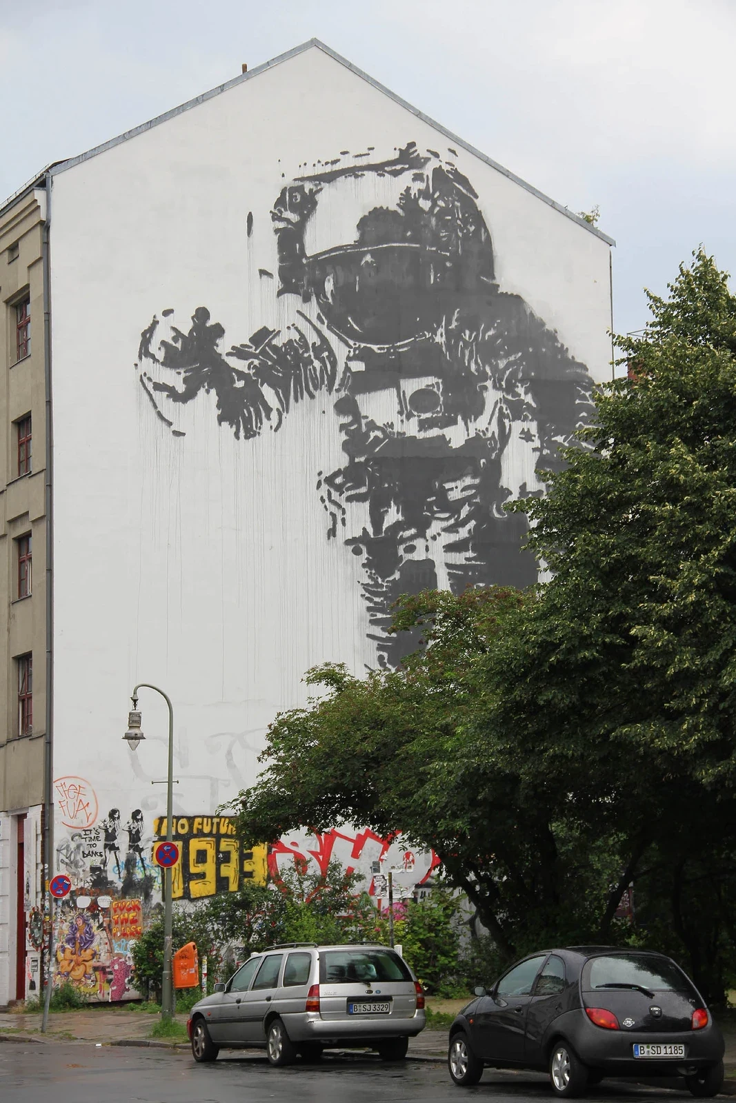 Un astronauta monocromo gigante ocupa una pared sobre árboles y coches aparcados.
