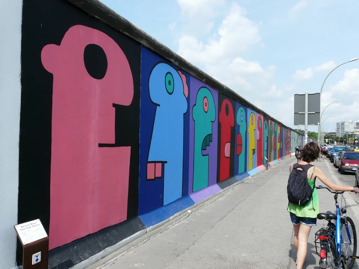 Perfiles coloridos de Thierry Noir se extienden por el Muro de Berlín junto a la acera.