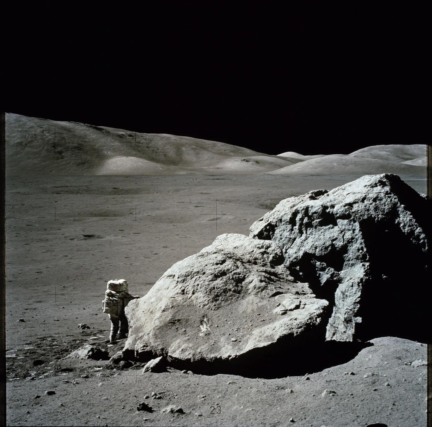 Harrison Schmitt stands beside a large split lunar boulder.
