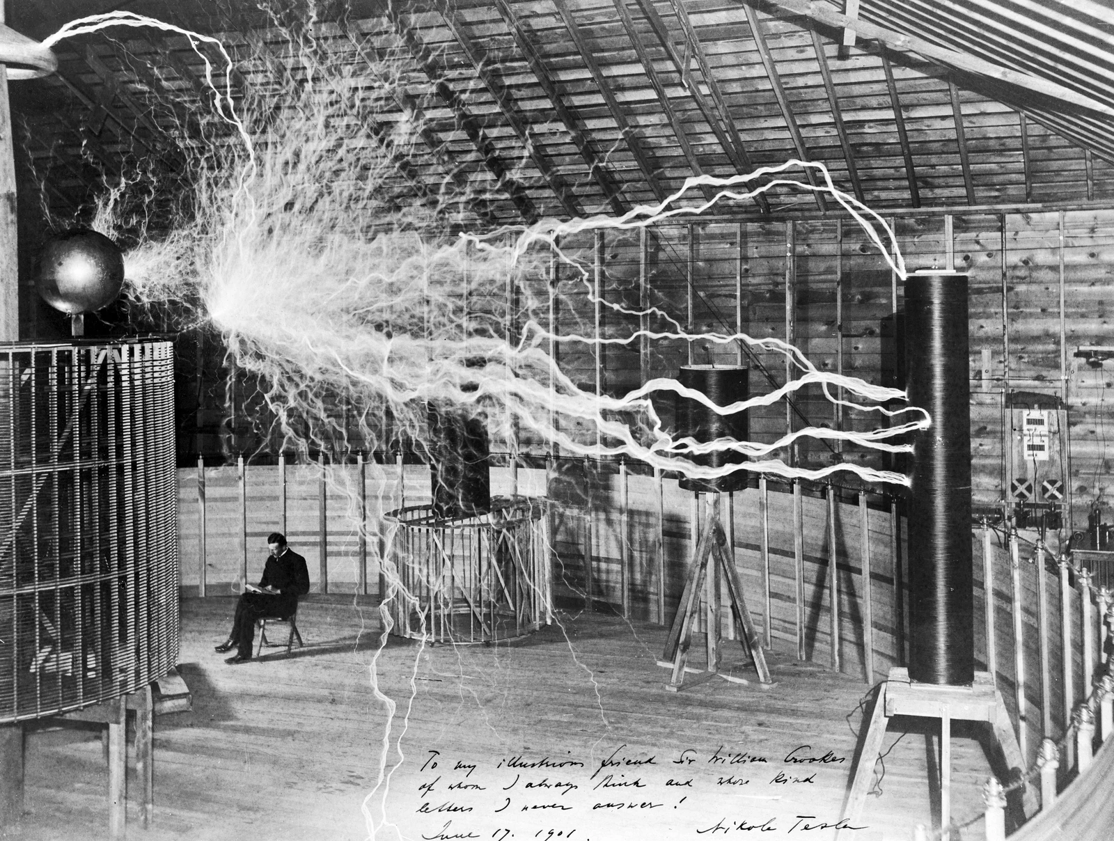 Photographie d’archives à double exposition réunissant Tesla assis et les décharges du laboratoire de Colorado Springs