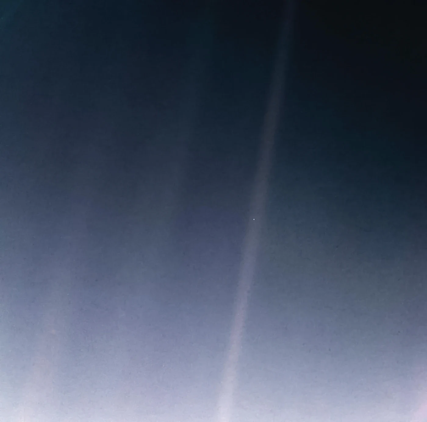 Earth appears as a tiny bright dot within a pale streak of scattered sunlight against dark space.